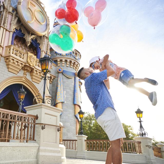 Father and son holding balloons in front of Cinderella's castle at Disney's Magic Kingdom® Park