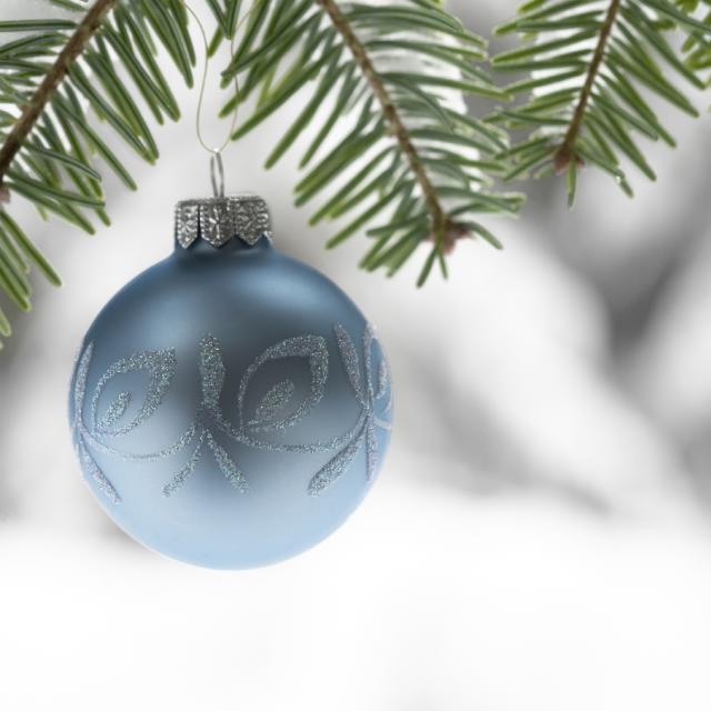 A blue Christmas ornament hanging on a pine tree