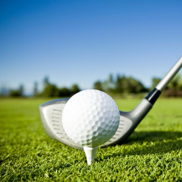 A close up of a golf ball on a tee and a golf club